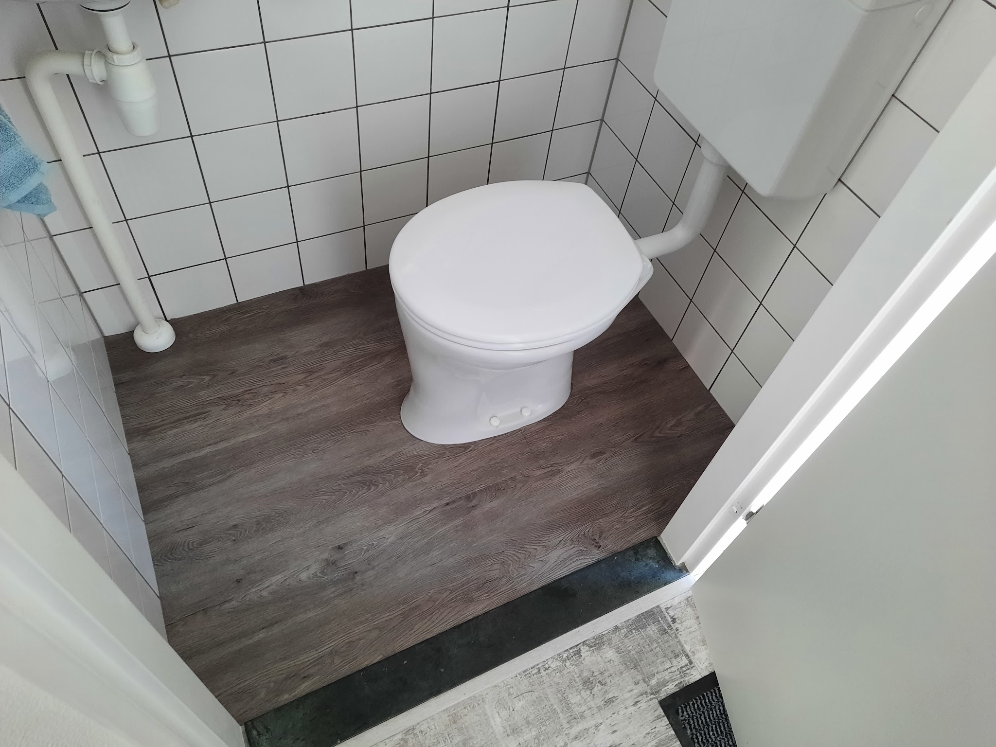 Donkere houtlook vloer in een kleine toiletruimte met witte tegels